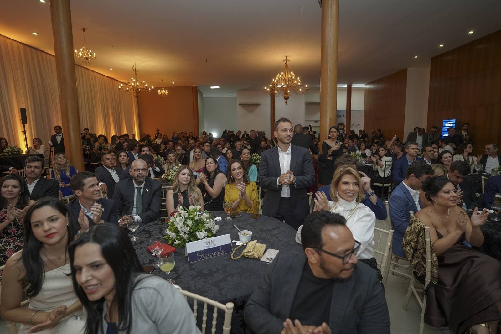 Plateia aplaude em pé e sentada nas mesas do salão iluminado por lustres, durante a cerimônia do Alvorada Business Awards